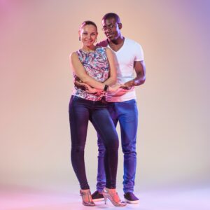 Young couple dances social Caribbean Salsa, studio shot on lilac background. Positive human emotions. The black african and caucasian models